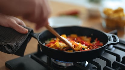 Una sartén llena de verduras mientras alguien cocina.