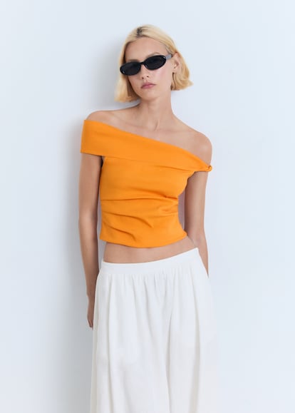 Con un patrón asimétrico que deja los hombros al descubierto, este top de Mango en tono naranja vitamina encapsula la energía del verano con un toque contemporáneo. Su diseño de tejido estructurado que se ajusta a la silueta es un buen contrapunto para pantalones holgados y faldas fluidas. (17.99  euros).