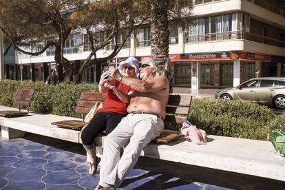 Una pareja sentada en uno de los bancos que se suceden a lo largo del paseo marítimo de Benidorm.