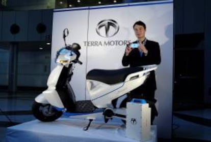 El presidente y fundador de Terra Motors Corporation, Toru Tokushige,  posa con un teléfono inteligente junto a una moto eléctrica "A4000i" durante la presentación del vehículo, en Tokio (Japón) hoy, miércoles 10 de julio de 2013.