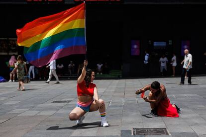 Un hombre toma una fotografía a una mujer que posa con una bandera LGBTI, en la plaza de Callao de Madrid