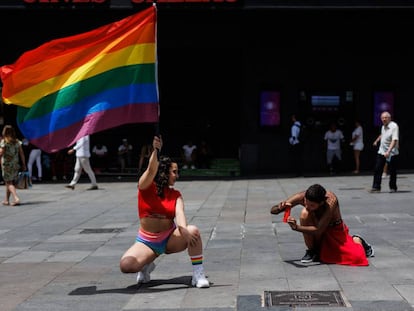 Un hombre toma una fotografía a una mujer que posa con una bandera LGBTI, en la plaza de Callao de Madrid