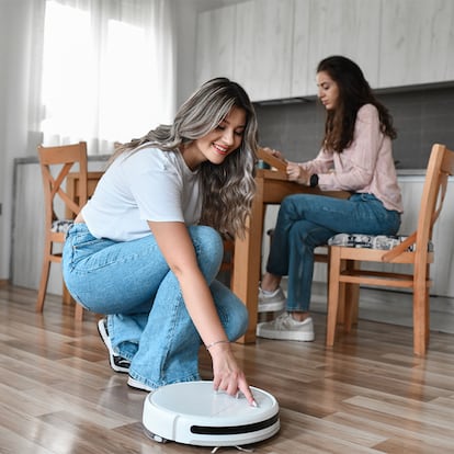 Una chica encendiendo el robot aspirador en la cocina de su casa.