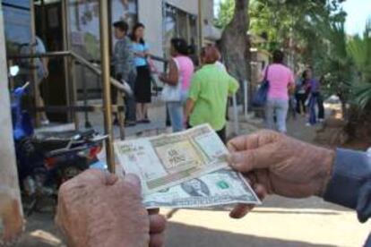 Un hombre muestra un peso convertible cubano y un dólar estadounidense frente a una oficina de la Western Union en La Habana (Cuba). EFE/Archivo