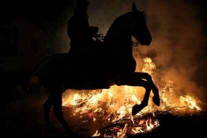 Las llamas resaltan la silueta de un caballo y su jinete durante la celebración de la luminarias.