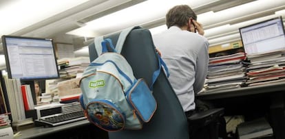 Un hombre trabaja en una oficina ante una mesa llena de documentos y con dos ordenadores.