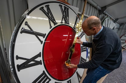 Un hombre sujeta la manecilla de un reloj de torre, en una foto de archivo.