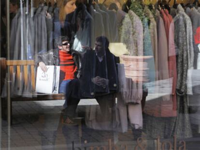 Dos clientes, reflejados en el escaparate de una tienda de ropa.