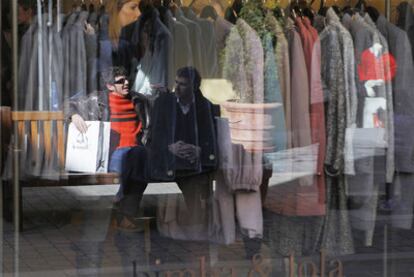 Dos clientes, reflejados en el escaparate de una tienda de ropa.