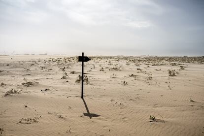 Abajo, una señal clavada en la arena, junto a la vía que recorre Mauritania de norte a sur, mientras se ve al fondo el puerto de Tanit.