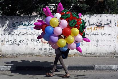 Un vendedor ambulante palestino lleva globos en una calle para vender.