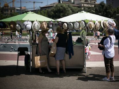 Varias personas compran sombreros para protegerse de la calor en plaza Catalunya de Barcelona.