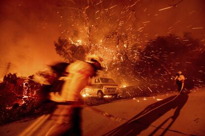 Una pareja de bomberos arrastra una manguera para sofocar el incendio declarado en Silverado, en el condado californiano de Orange.