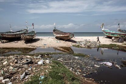 Un hombre camina entre viejos barcos de pesca a lo largo de la costa de Bargny el 15 de agosto de 2020. Esta población cuenta con unos 70.000 habitantes, la mayoría de origen lebu, comunidad tradicionalmente compuesta por agricultores y pescadores.