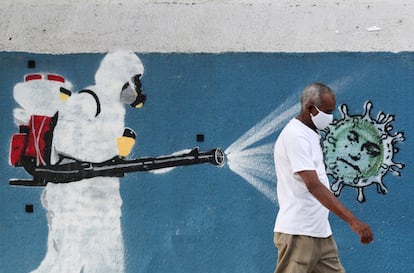 Um homem usando máscara de proteção passa por um mural com referência à pandemia no Rio de Janeiro, em 12 de junho.