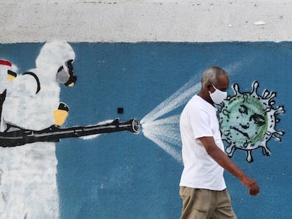 Um homem usando máscara de proteção passa por um mural com referência à pandemia no Rio de Janeiro, em 12 de junho.