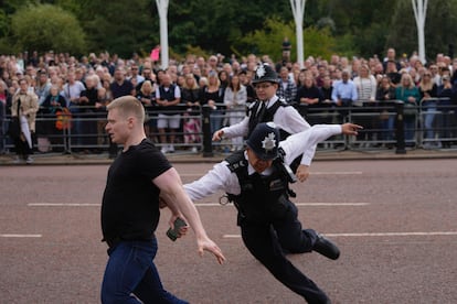 Police officers chase a man who jumped a barrier moments before Charles III's car arrived at Buckingham Palace. 