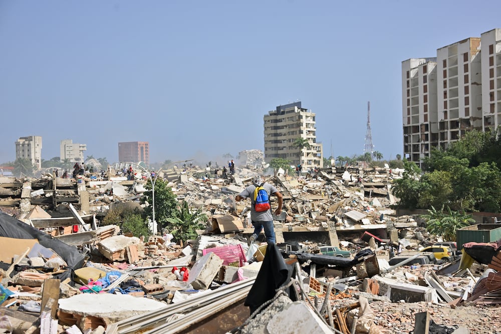 A man with a Venezuelan flag-themed backpack walks amid rubble of collapsed buildings after earthquakes hit the country, in La Guaira, Venezuela, June 26, 2026. REUTERS/Maxwell Briceno