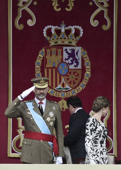 El Rey saluda desde la tribuna. A su lado, la Reina con el pelo recogido en un moño bajo.