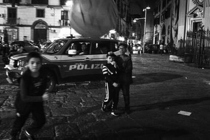 Um grupo de crianças brinca na praça da igreja de San Vincenzo, tarde da noite, em frente ao carro da patrulha policial.