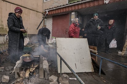 Varias personas cocinan en una fogata en el exterior de un edificio de apartamentos sin electricidad, agua ni gas desde el comienzo de la invasión rusa, en Bucha.