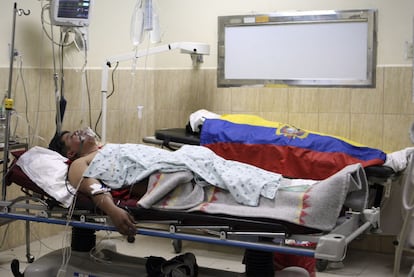 Un policía herido yace en el hospital junto al cuerpo de un compañero tapado con una bandera de Ecuador.