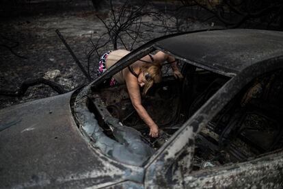 Una mujer coge papeles en el interior de su vehículo calcinado tras el incendio forestal en la ciudad griega de Mati.