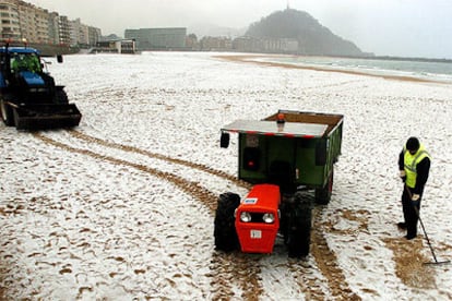 Operarios del servicio de limpieza trabajan en la playa de la Zurriola de San Sebastián, cubierta de nieve.