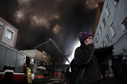 Un niño habla por teléfono mientras los bomberos extinguen un almacén en llamas en el sur de Moscú, este viernes.
