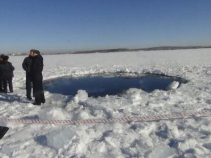 Unos hombres pasean al lado de un agujero de ocho metros en el lugar donde un meteorito impactó, en el lago congelado Chebarkul, Rusia