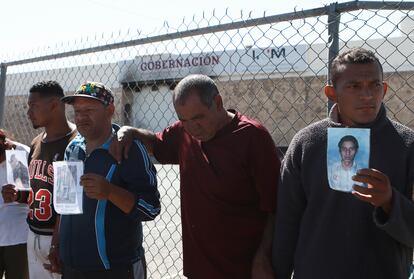 Migrants, mostly from Venezuela, hold photos of those who died in a fire at a Mexican immigration detention center, behind, during a prayer vigil outside the center in Ciudad Juarez, Mexico, April, 27, 2023