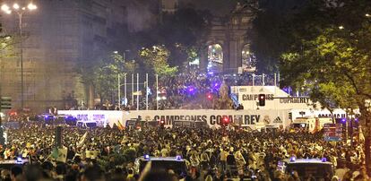 Miles de hinchas del Real Madrid rodean la fuente de Cibeles, vallada y protegida por la policía, con la Puerta de Alcalá al fondo.