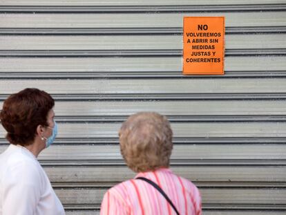 Dos mujeres leen un cartel puesto en una persiana echada de un comercio de Málaga en el que se puede leer: "No volveremos a abrir sin medidas justas y coherentes", este viernes.