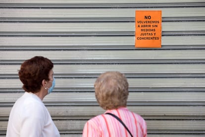 Dos mujeres leen un cartel puesto en una persiana echada de un comercio de Málaga en el que se puede leer: "No volveremos a abrir sin medidas justas y coherentes", este viernes.