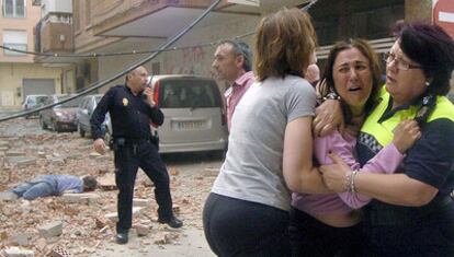 Una policía y una vecina consuelan a una mujer, en la calle de Galicia en Lorca, donde una víctima yace entre los escombros.