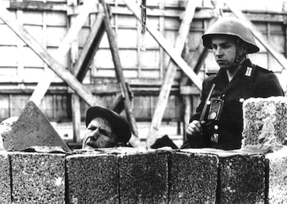 Un soldado de la Alemania Oriental observa cómo un obrero coloca ladrillos del nuevo muro de Berlín el día en el que este empezó a construirse, el 12 de agosto de 1961.