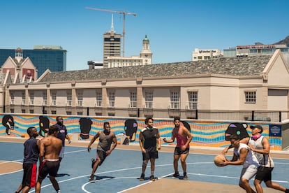 Unos chicos juegan un partido de baloncesto en el área Victoria & Albert Waterfront de Ciudad del Cabo, Sudáfrica, en diciembre de 2020, al comienzo de la segunda ola de covid-19 en este país. Pincha en la imagen para ver la fotogalería completa.