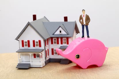 Miniature house and small piggy bank against white