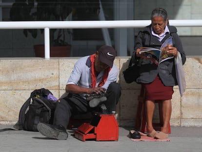 Una mujer lee una revista mientras un hombre bolea sus zapatos, en Oaxaca.