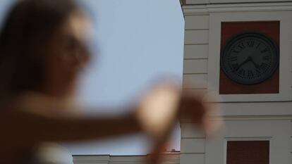 Una joven mira su reloj de muñeca frente al de la puerta del Sol.