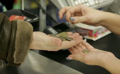 Una cajera ayuda a un cliente a contar las monedas de euro en un supermercado.