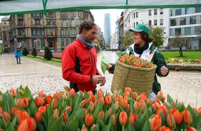 Una joven reparte tulipanes en la Plaza Moyúa con la sede de Iberdrola al fondo.