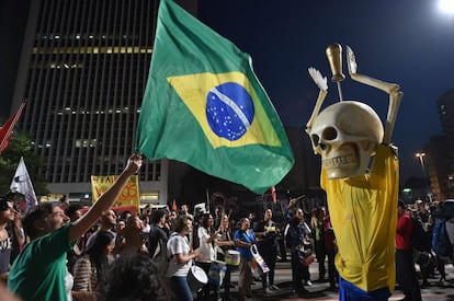 Homem segura bandeira do Brasil diante de boneco de esqueleto em manifestação em São Paulo.