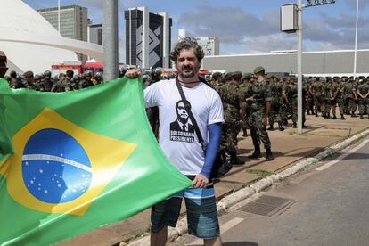 Eleitor de Bolsonaro posa com uma bandeira do Brasil diante do ensaio do esquema de segurança da posse.