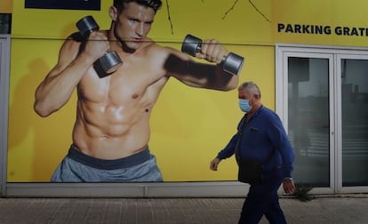 Un hombre, con mascarilla, pasa delante de un cartel de publicidad de un gimnasio en Rubí (Barcelona).