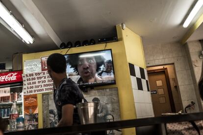 Un solicitante de asilo mira la televisión israelí, en la que aparece un cómico con la cara pintada de negro, en un restaurante de falafel de Tel Aviv. En general, la sociedad israelí discrimina a los solicitantes de asilo, que permanecen atrapados en un limbo legal, sin que las instituciones del Estado los reconozcan como tales.