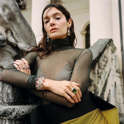 Sujetador de ZARA, cuello cisne de tul de seda nude y cuello cisne de tul de seda verde de CORTANA, falda de punto elástico de ERNESTO NARANJO y joyas de la colección alta joyería Mediterranea de BVLGARI: pendientes en oro amarillo con 4 piedras (turmalina verde, citrino, aguamarina, amatista), 4 espinelas redondas, 4 diamantes redondos talla brillante y diamantes engastados en pavé, anillo en platino con 1 zafiro, 28 esmeraldas buff-top, 2 diamantes redondos talla brillante y diamantes engastados en pavé, anillo en oro rosa con elementos de turquesa, 1 morganita, 2 diamantes talla brillante redondos y diamantes engastados en pavé. En la otra mano, pulsera en oro amarillo con 8 rubelitas cabujón, 8 amatistas cabujón, 8 esmeraldas cabujón, diamantes talla brillante redondos y diamantes engastados en pavé y anillo en platino con 1 esmeralda, 12 diamantes talla fantasía y diamantes engastados en pavé.