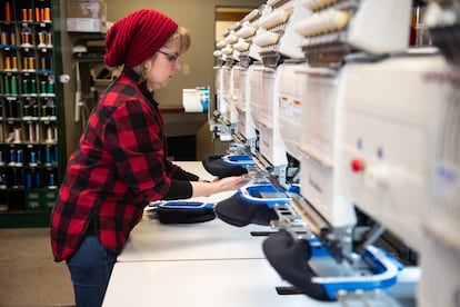 Stephanie Maher, an employee of The Sam Group LTD, a textile factory in Ottawa, loads a machine to embroider the caps with the message "Canada is Not for Sale."