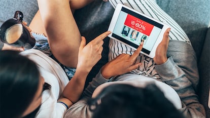 Dos chicas mirando rebajas en la tablet desde el sofá de su casa.