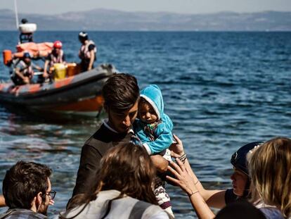 Varios voluntarios ayudan a un inmigrante afgano tras llegar con un bebé a la isla de Lesbos.